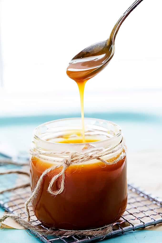 a spoon holding some caramel sauce being lifted up from a jar of caramel sauce.