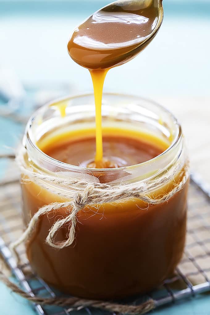 a spoon lifting a spoon of caramel sauce from a jar of caramel sauce on a cooling rack.