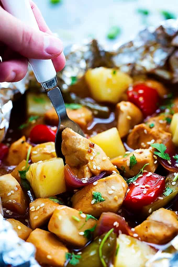 close up of a hand grabbing a bite of a pineapple chicken foil packet with a fork.