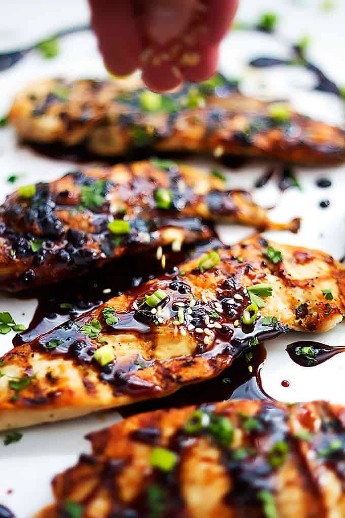 a hand sprinkling seasoning on top of sticky Asian grilled chicken.