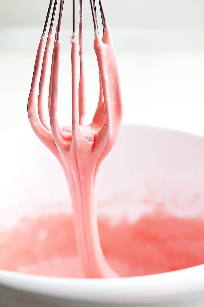 a whisk being lifted up from a bowl of strawberry lemonade donut batter.