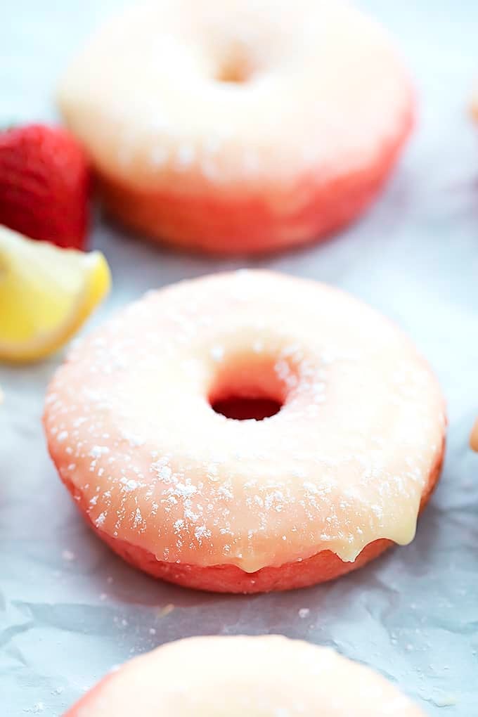 a strawberry lemonade donut with a strawberry, slice of a lemon and another donut in the background.