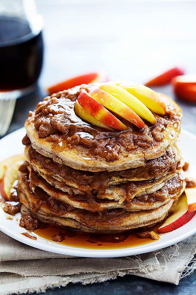 a stack of apple cinnamon streusel pancakes on a plate topped with syrup, buttery cinnamon streusel topping and apples.