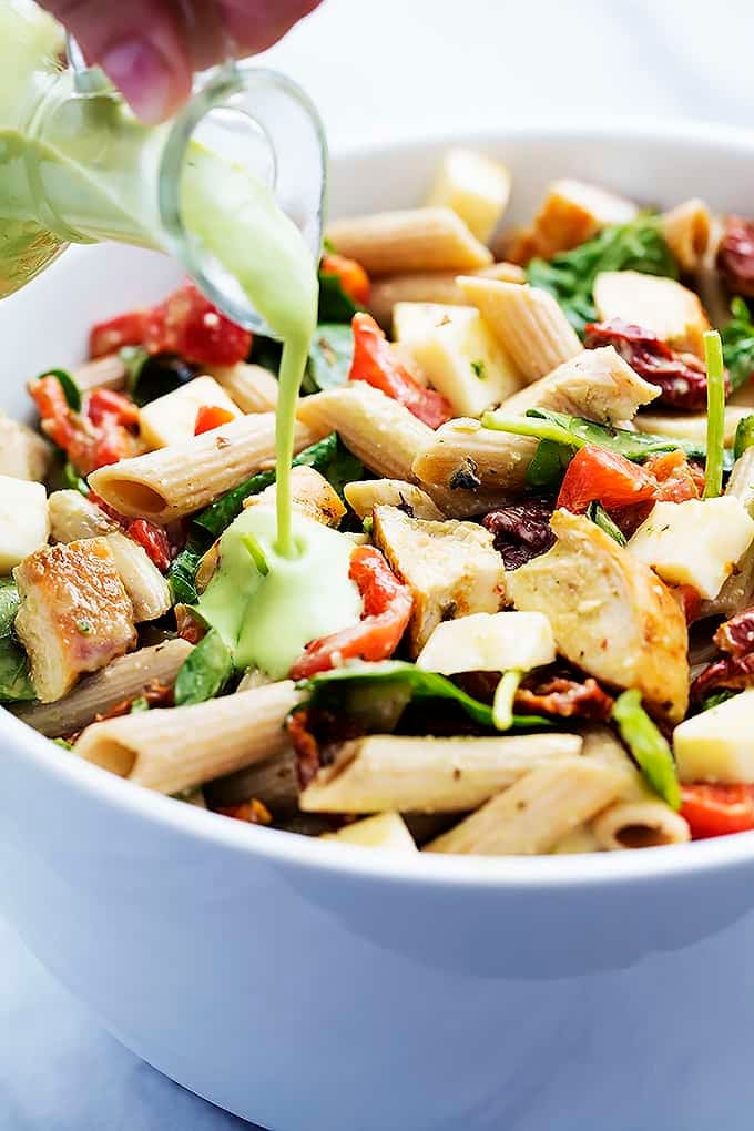 chicken penne salad in a bowl with creamy parmesan dressing being poured on top.