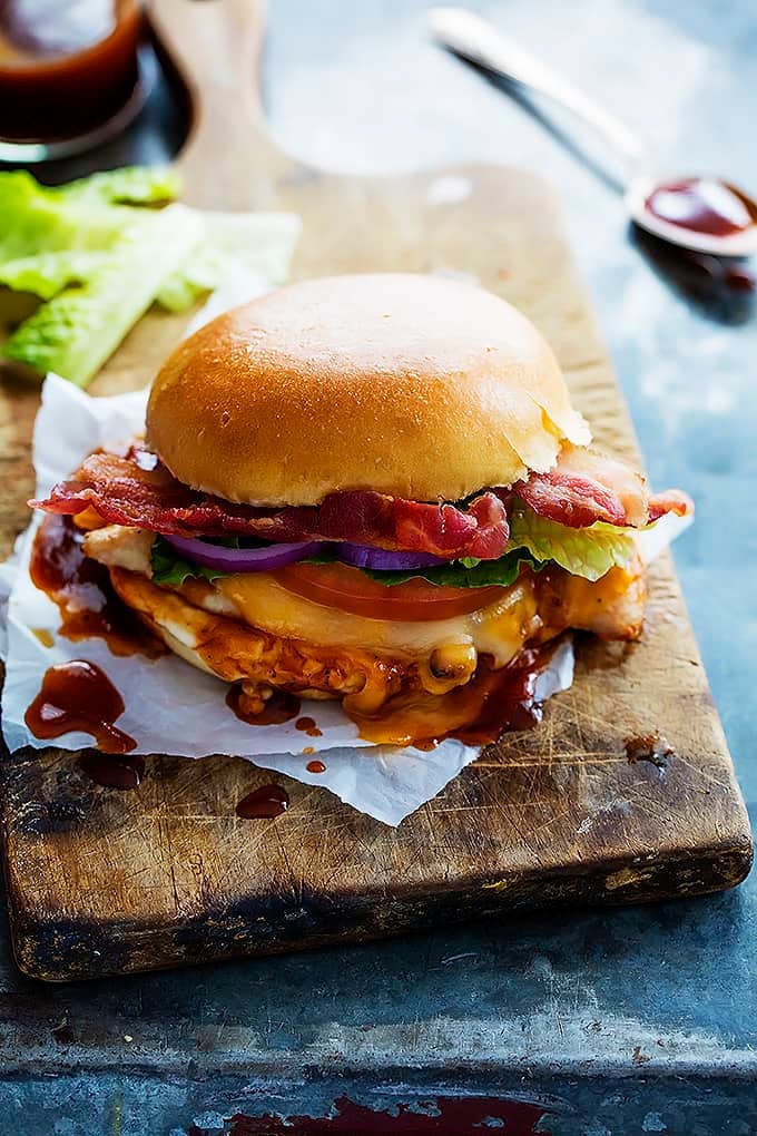 a monterey chicken sandwich on a wooden cutting board with a jar and spoon with sauce in/on them.