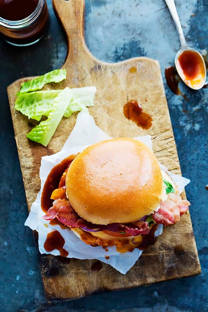 top view of a monterey chicken sandwich on a wooden cutting board with a spoon and jar of sauce on the side.