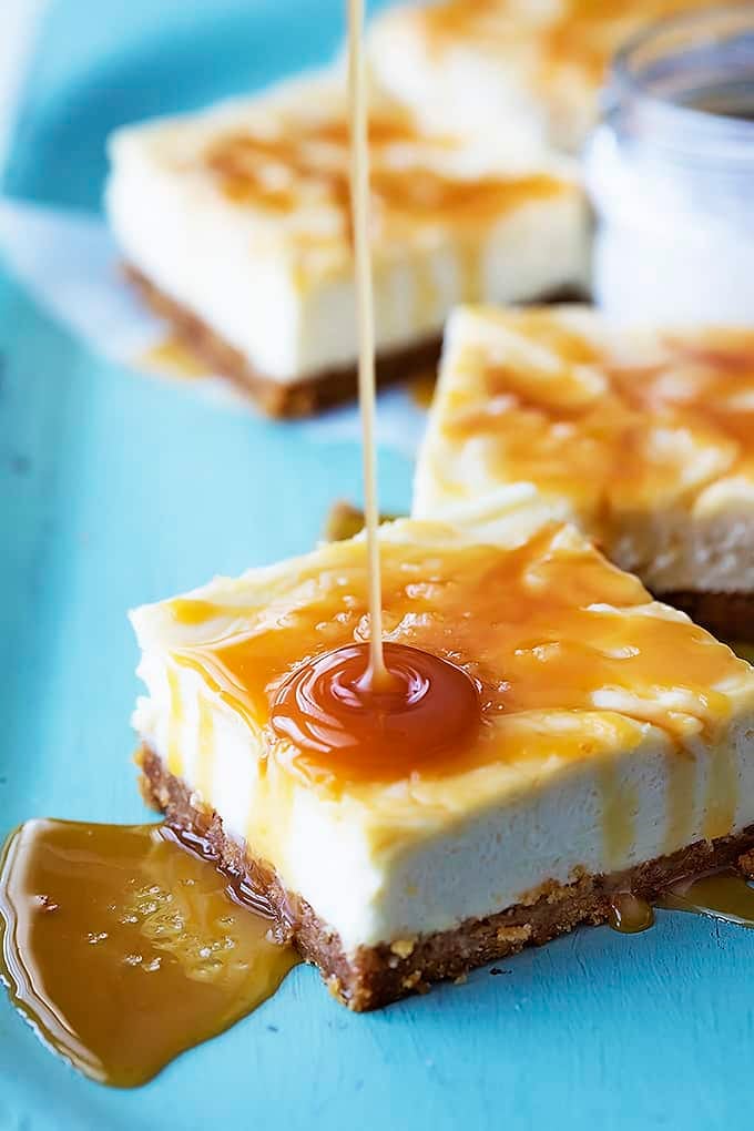 salted caramel cheesecake bars with caramel sauce being poured on top of the bar in the front.