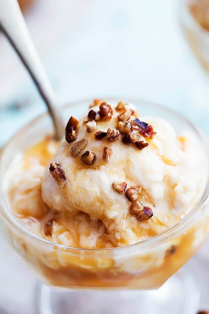 close up of no churn salted caramel ice cream with a spoon in a sundae glass topped with nuts and caramel sauce.