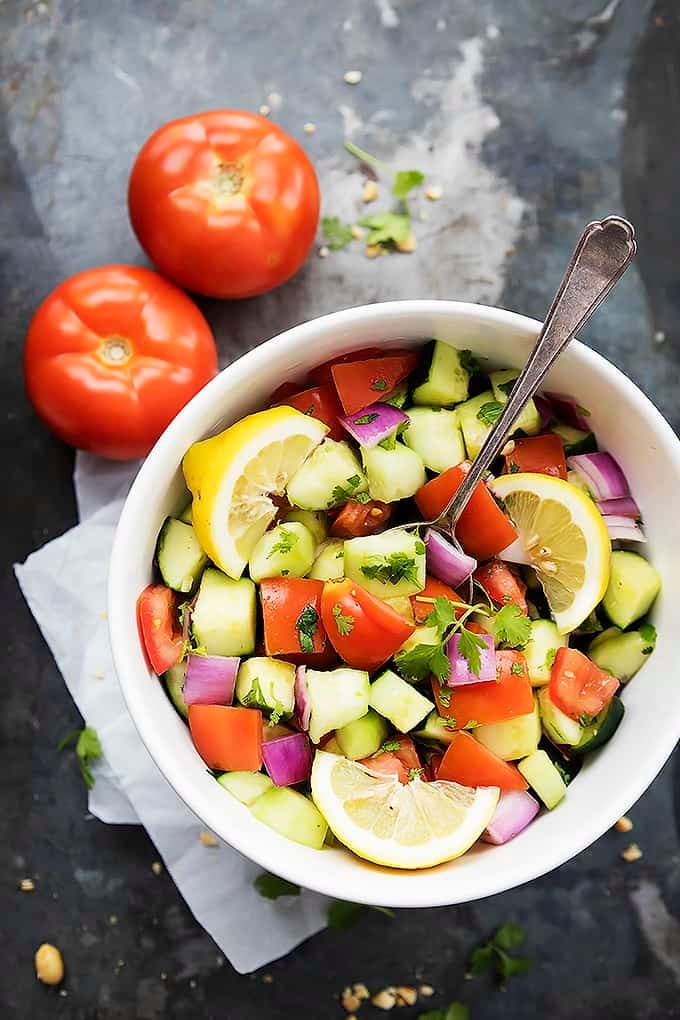 top view of a bowl of tomato cucumber salad with a spoon with tomatoes on the side.