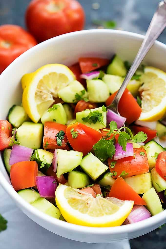 close up of tomato cucumber salad with a spoon in a bowl with tomatoes in the background.