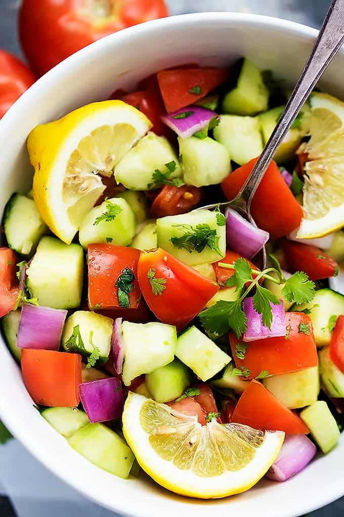 close up top view of tomato cucumber salad with a spoon in a bowl.