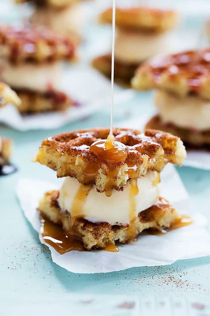 a snickerdoodle waffle ice cream sandwich with caramel sauce being poured on top with more sandwiches in the background.