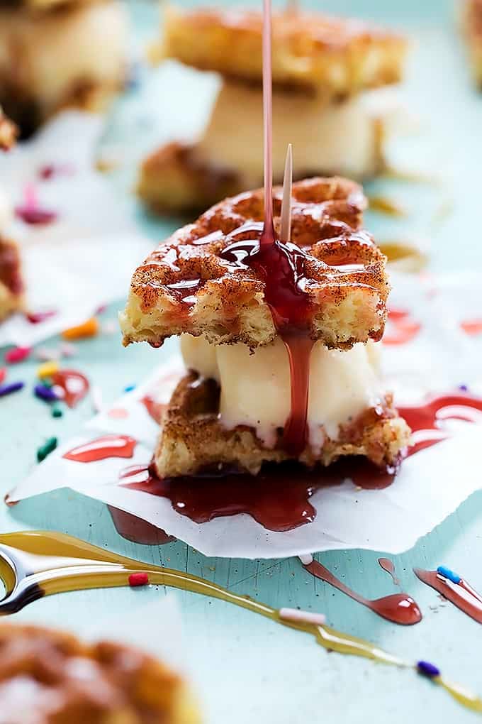 a snickerdoodle waffle ice cream sandwich with strawberry sauce being poured on top.