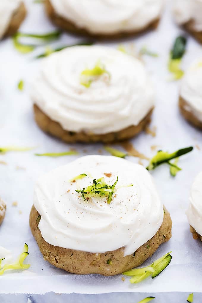 zucchini cookies with brown butter cream cheese frosting topped with zucchini shavings and surrounded by more shavings.