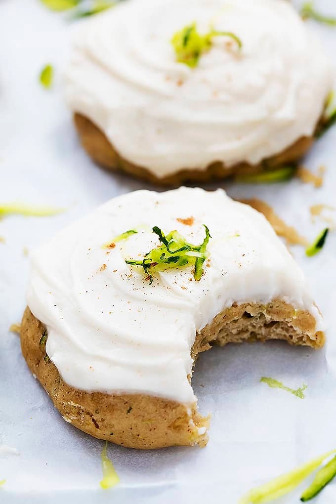 a zucchini cookie with brown butter cream cheese frosting with a bite missing and another cookie in the background.