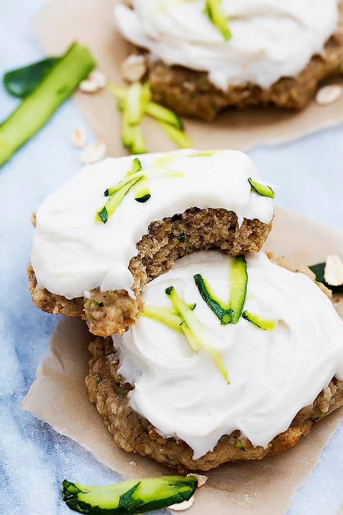 stacked frosted zucchini oatmeal cookies with the top cookie having a bite missing.