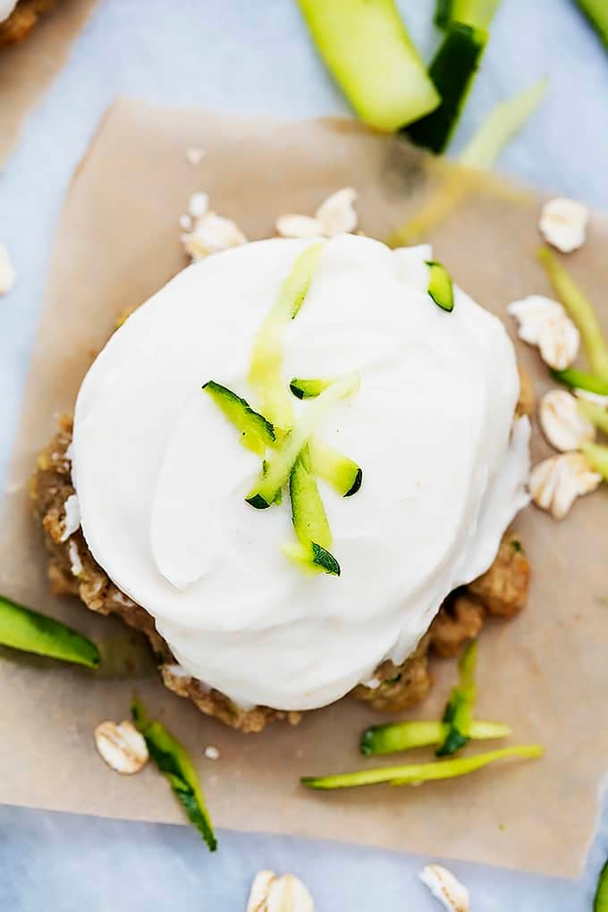 top view of a frosted zucchini oatmeal cookie surrounded by oats and zucchini shavings.