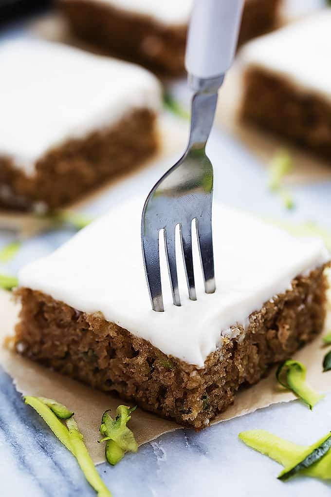 a piece of zucchini sheet cake with a fork in it with more pieces in the background.