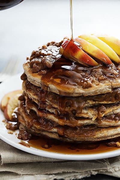 apple cinnamon streusel pancakes on a plate with syrup being poured on top.