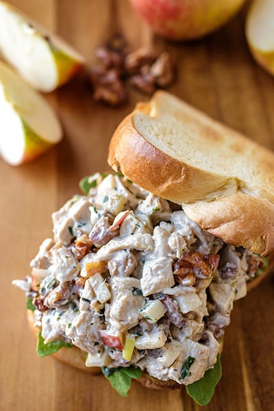 apple candied walnut chicken salad on a piece of bread with another piece of bread resting on the side of the sandwich.