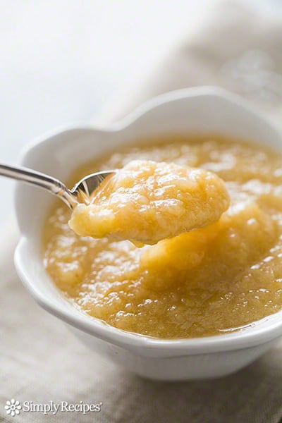 a spoon lifting a spoonful of homemade apple sauce from a bowl.