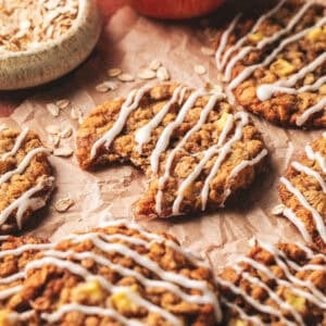 Apple oatmeal cookies on parchment paper with a bite out of one.