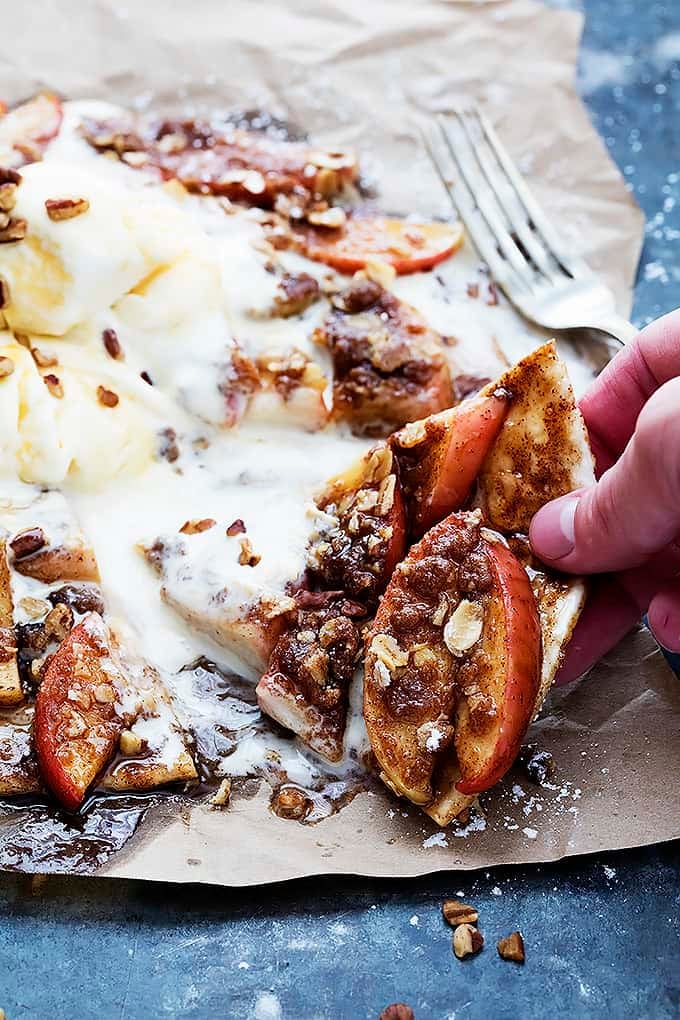 a hand picking up a piece of apple crumble flatbread with a fork on the side.