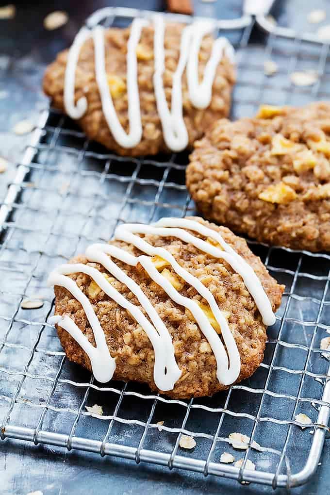 apple oatmeal cookies on a cooling rack with some drizzled with apple cream cheese frosting.