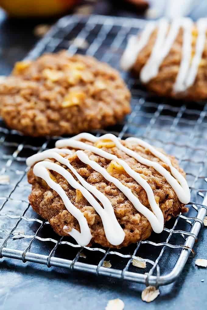 apple oatmeal cookies on a cooling rack with some drizzled with apple cream cheese frosting.