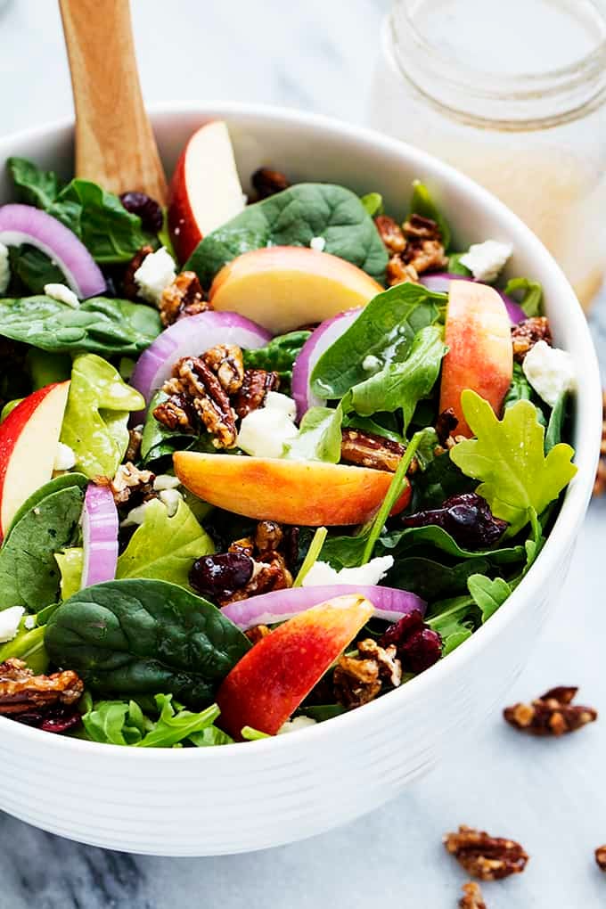 apple pecan salad with maple vinaigrette and a wooden serving spoon in a bowl with more vinaigrette in a mason jar on the side.