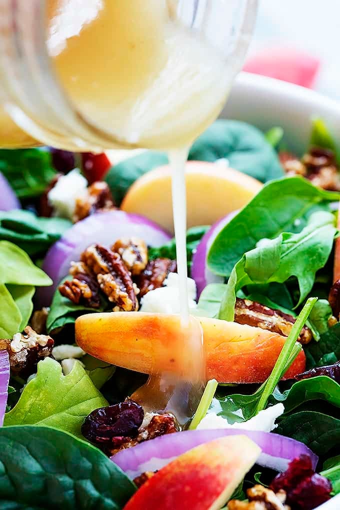 close up of maple vinaigrette being poured on top of apple pecan salad.