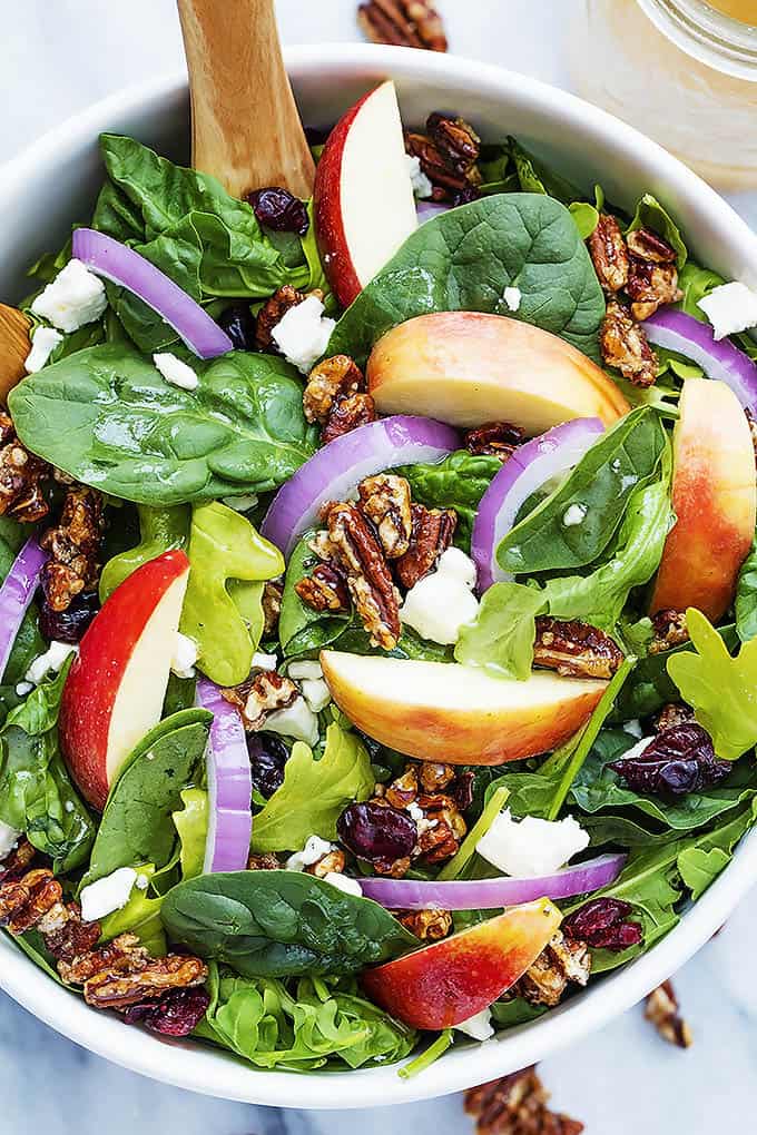 top view of apple pecan salad with maple vinaigrette and a wooden serving spoon in a bowl.