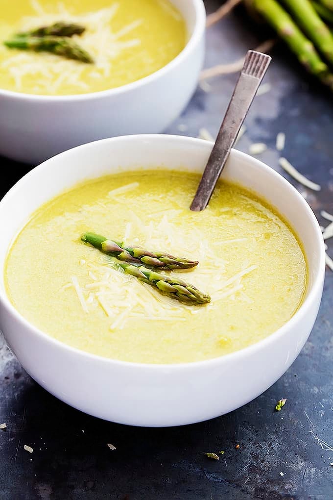 asparagus parmesan soup and a spoon in a bowl with another bowl of soup in the background.