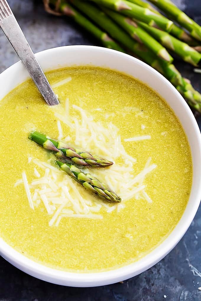 close up top view of asparagus parmesan soup with a spoon in a bowl with asparagus on the side.