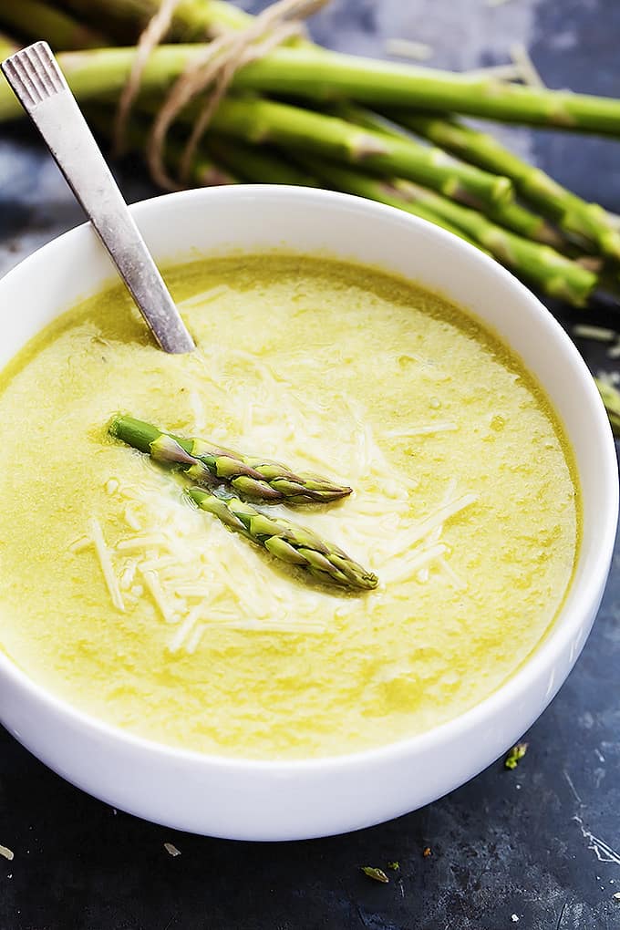 asparagus parmesan soup and a spoon in a bowl with asparagus stalks in the background.