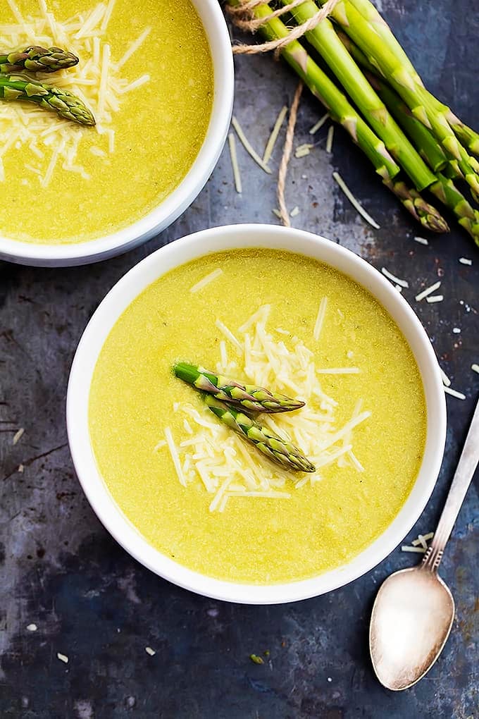 top view of two bowls of asparagus parmesan soup with asparagus and a spoon on the side.