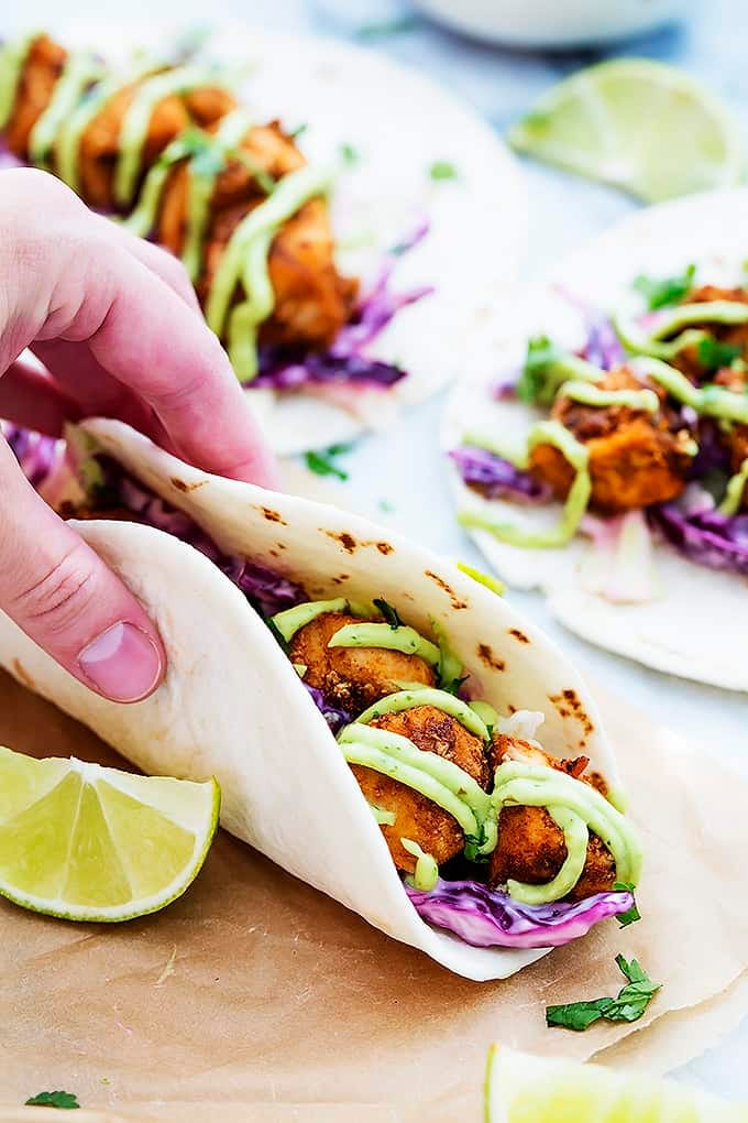 a hand picking up a baja fish taco with more tacos in the background.