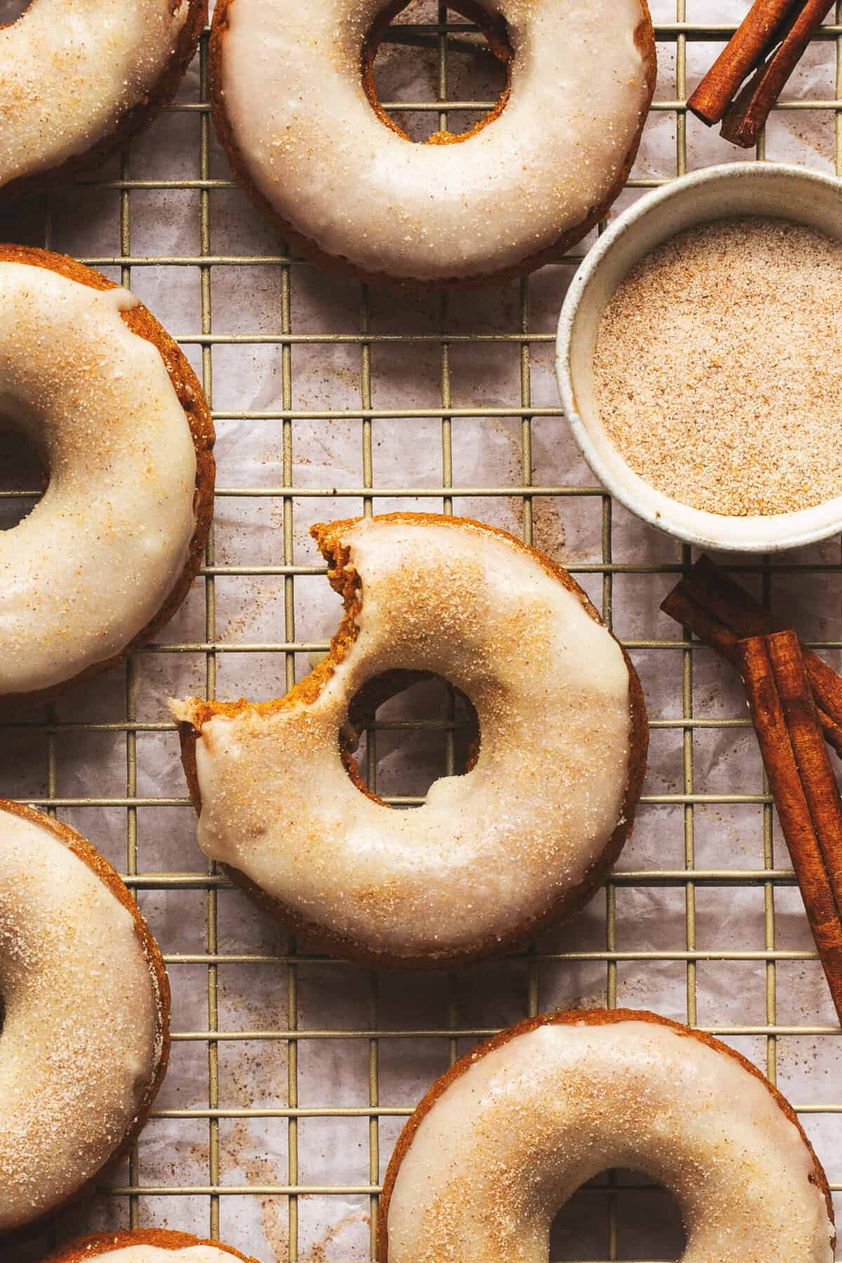 Overhead of baked pumpkin donuts on a cooling rack with one missing a bite.