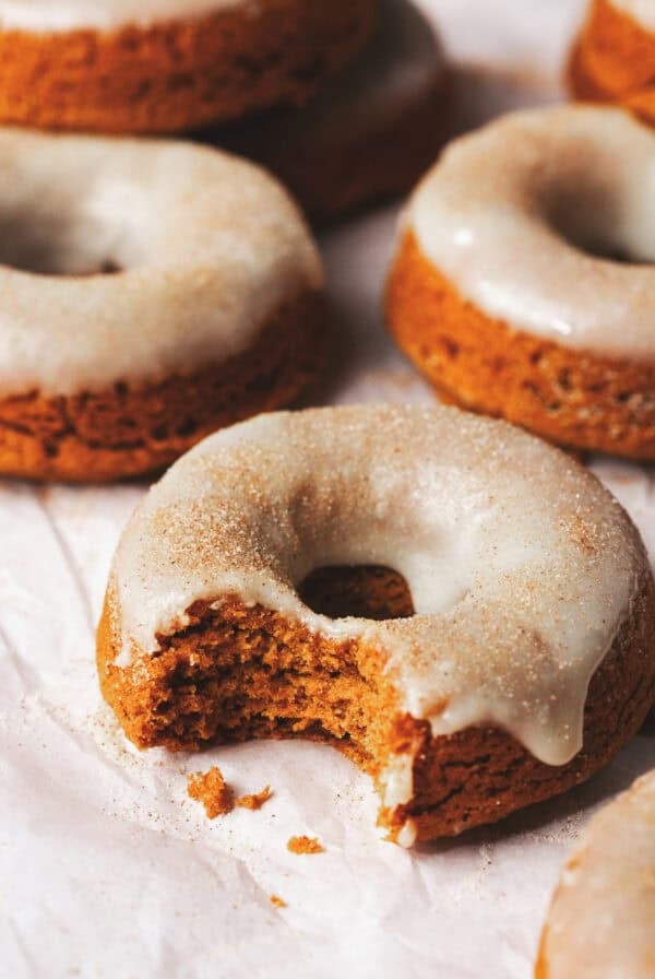 Close up of baked pumpkin donuts with a bite missing from the one in front.