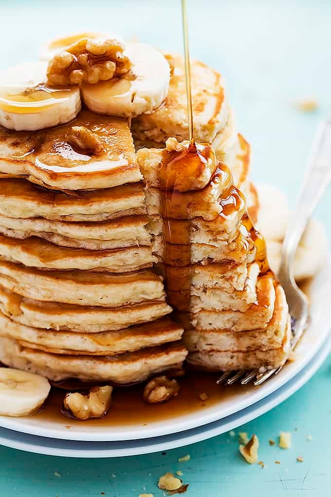 a stack of banana bread pancakes with a bite separated from the rest of the stack sitting on top of a fork with syrup being poured on top.