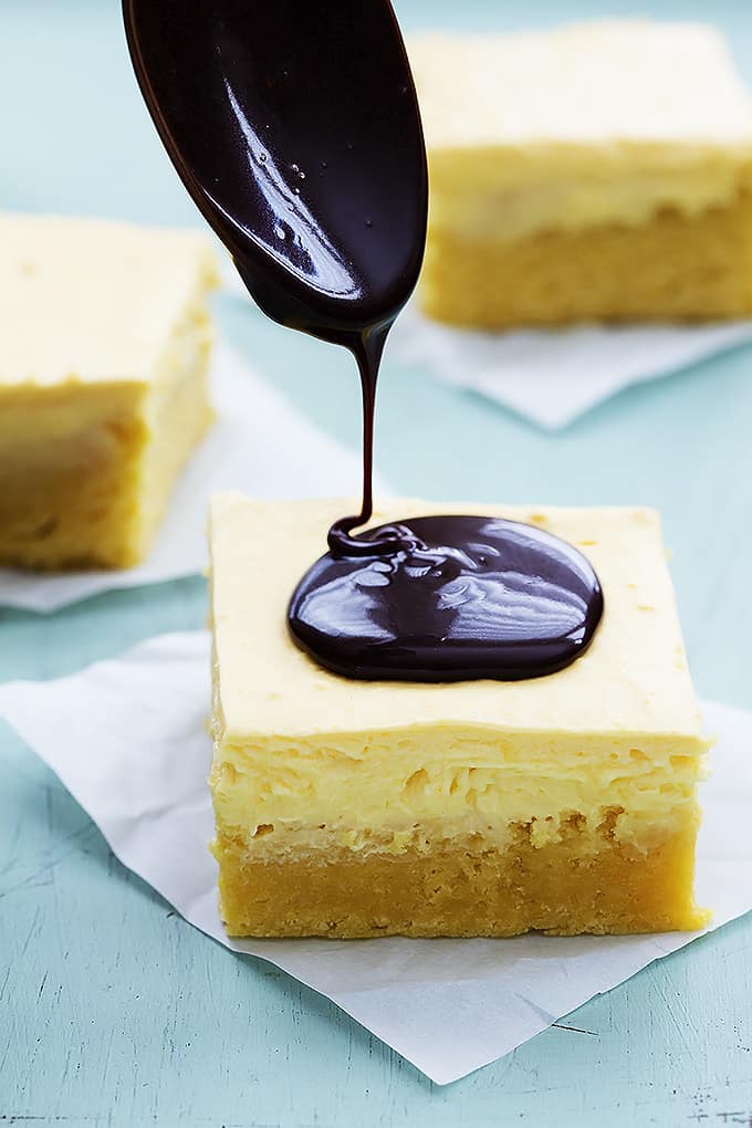 chocolate ganache being poured on top of a Boston cream pie bar with more bars in the background.