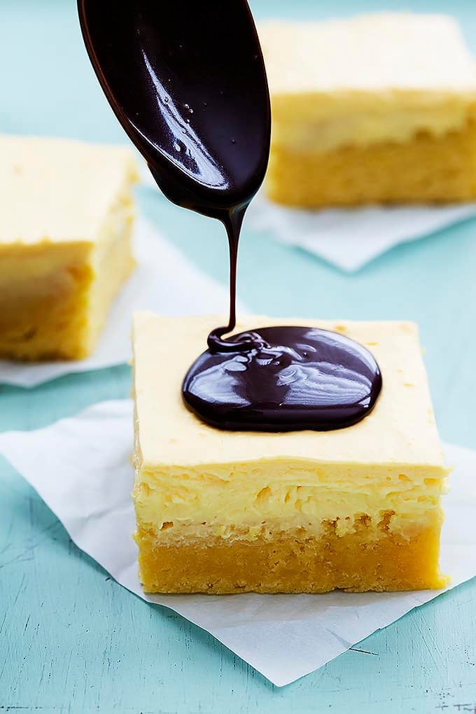 chocolate ganache being poured on top of a Boston cream pie bar with more bars in the background.