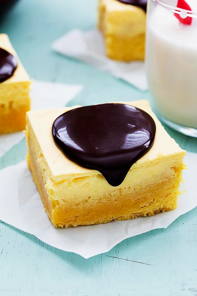 a Boston cream pie bar with chocolate ganache on top with more bars with ganache and a glass of milk in the background.