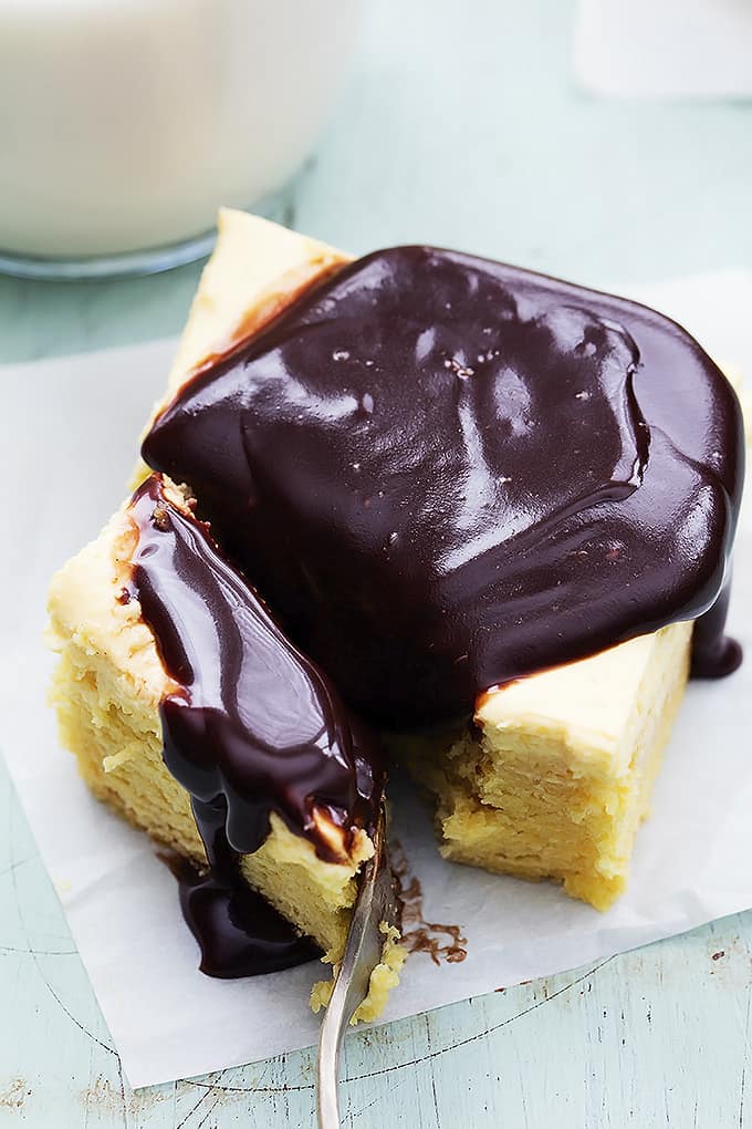 close up of a fork cutting a bite of a Boston cream pie bar with chocolate ganache on top.