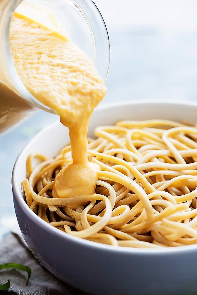 close up of butternut squash pasta sauce being poured on top of a bowl of pasta.