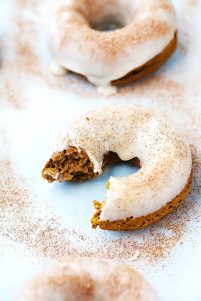 close up of a baked pumpkin donut with a bite missing with another donut on the side.