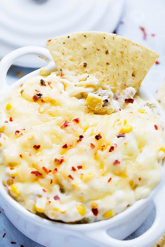 hot cheesy corn dip in a bowl with a chip dipped in it.