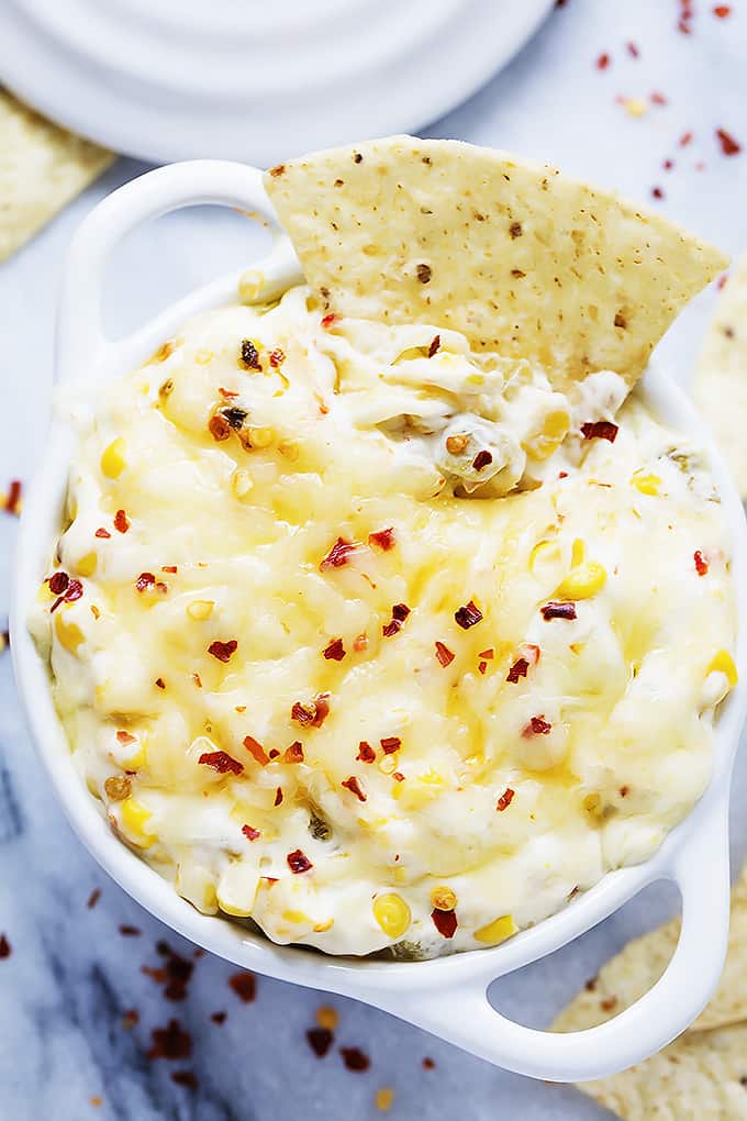 top view of a bowl of hot cheesy corn dip with a chip dipped in it.