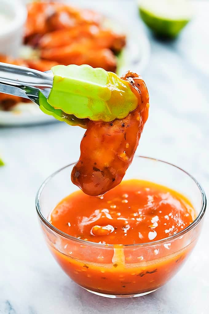 tongs holding up a spicy honey lime chicken wing just dipped in spicy honey lime sauce.
