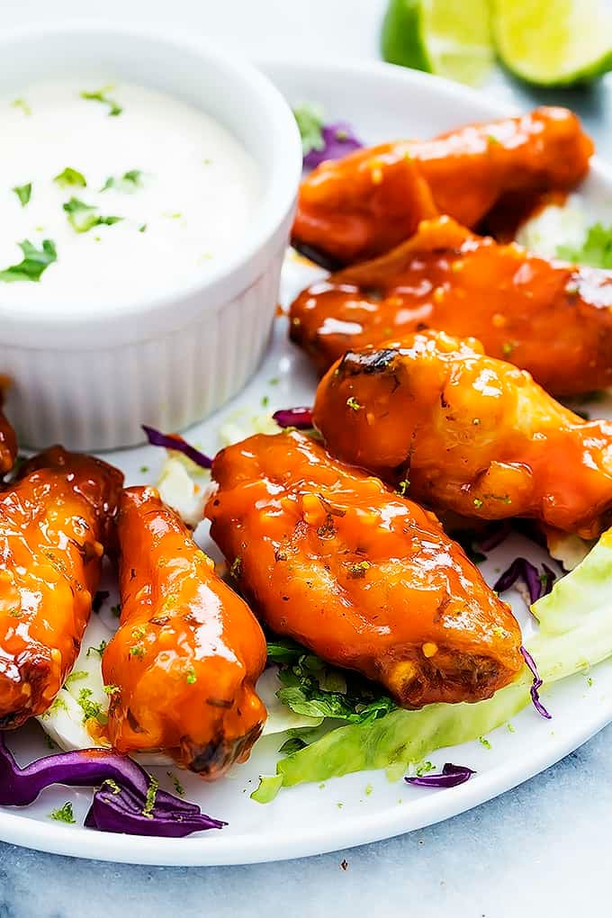 spicy honey lime chicken wings next to a bowl of dipping sauce on a plate.